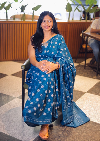 Woman in a blue saree sitting on a chair indoors.