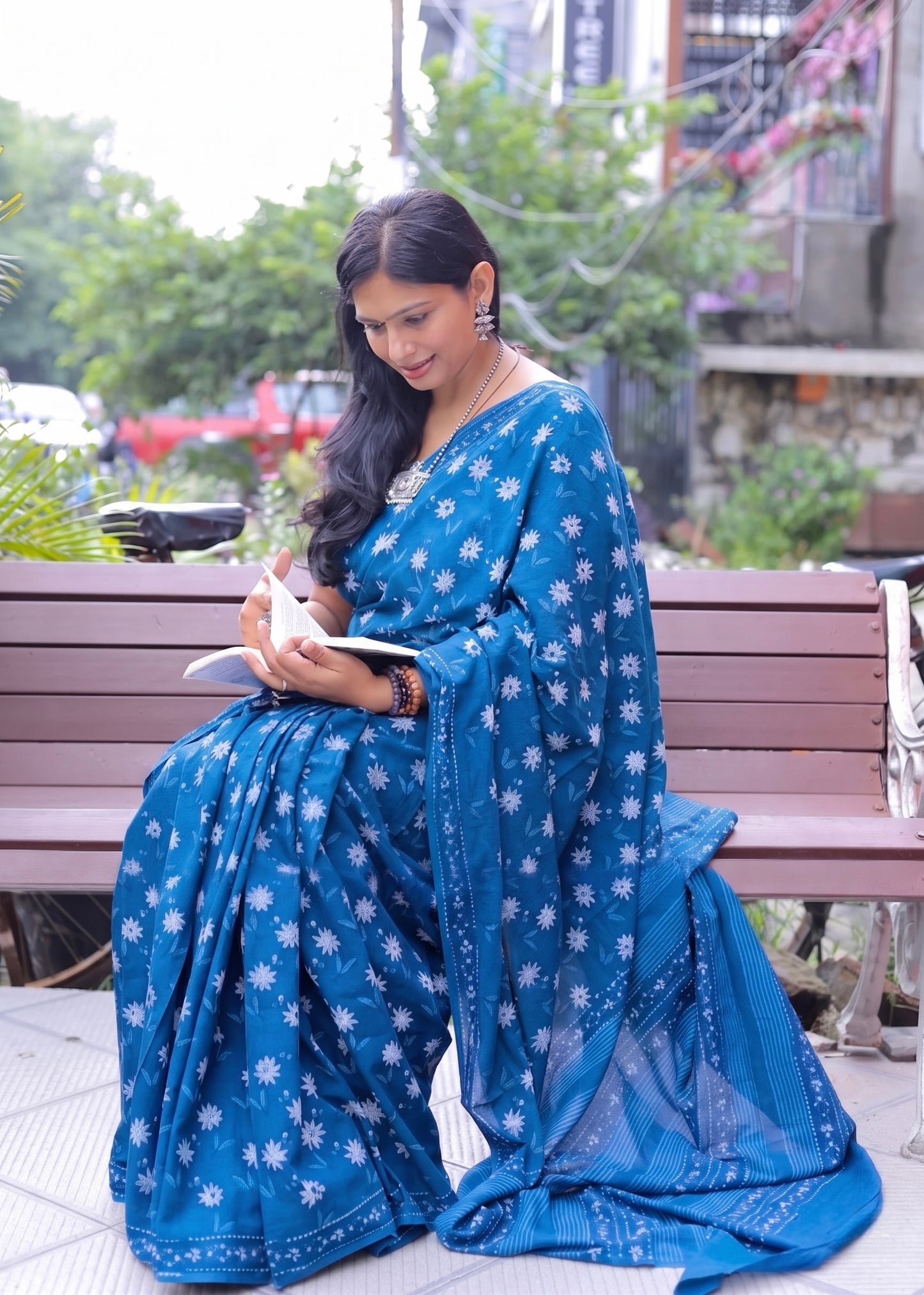 Woman in a blue saree sitting on a bench outdoors