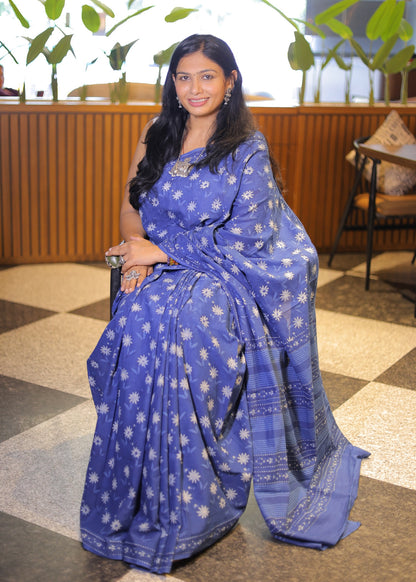 Woman wearing a blue saree with white patterns in an indoor setting.