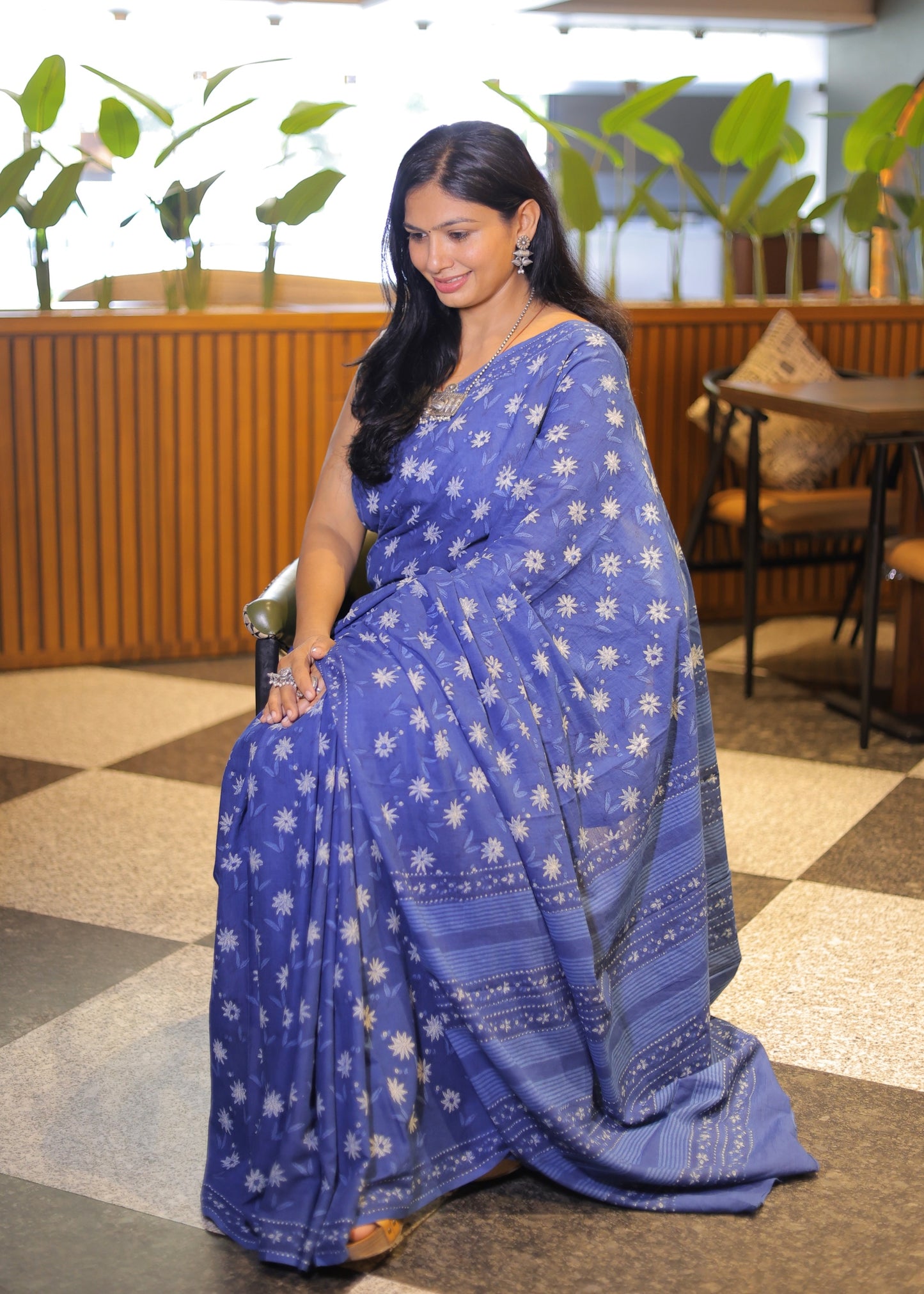Woman wearing a blue saree with white patterns in an indoor setting.