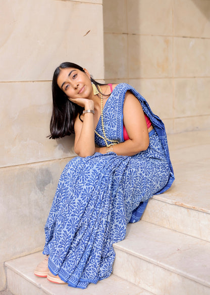 Woman in a blue saree sitting on steps with a neutral background