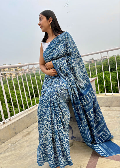 Woman wearing a blue patterned saree on a rooftop with greenery in the background