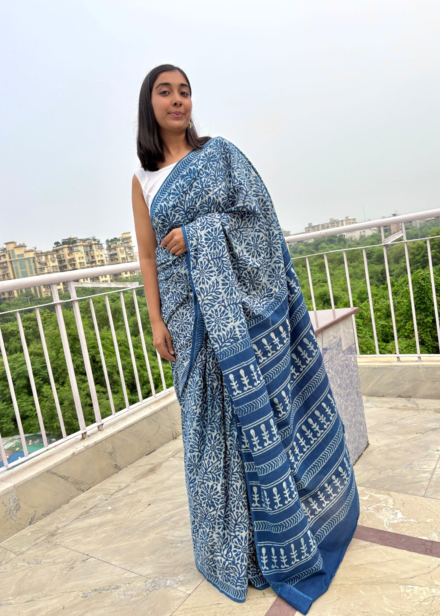 Woman wearing a blue and white patterned saree on a rooftop with a cityscape background